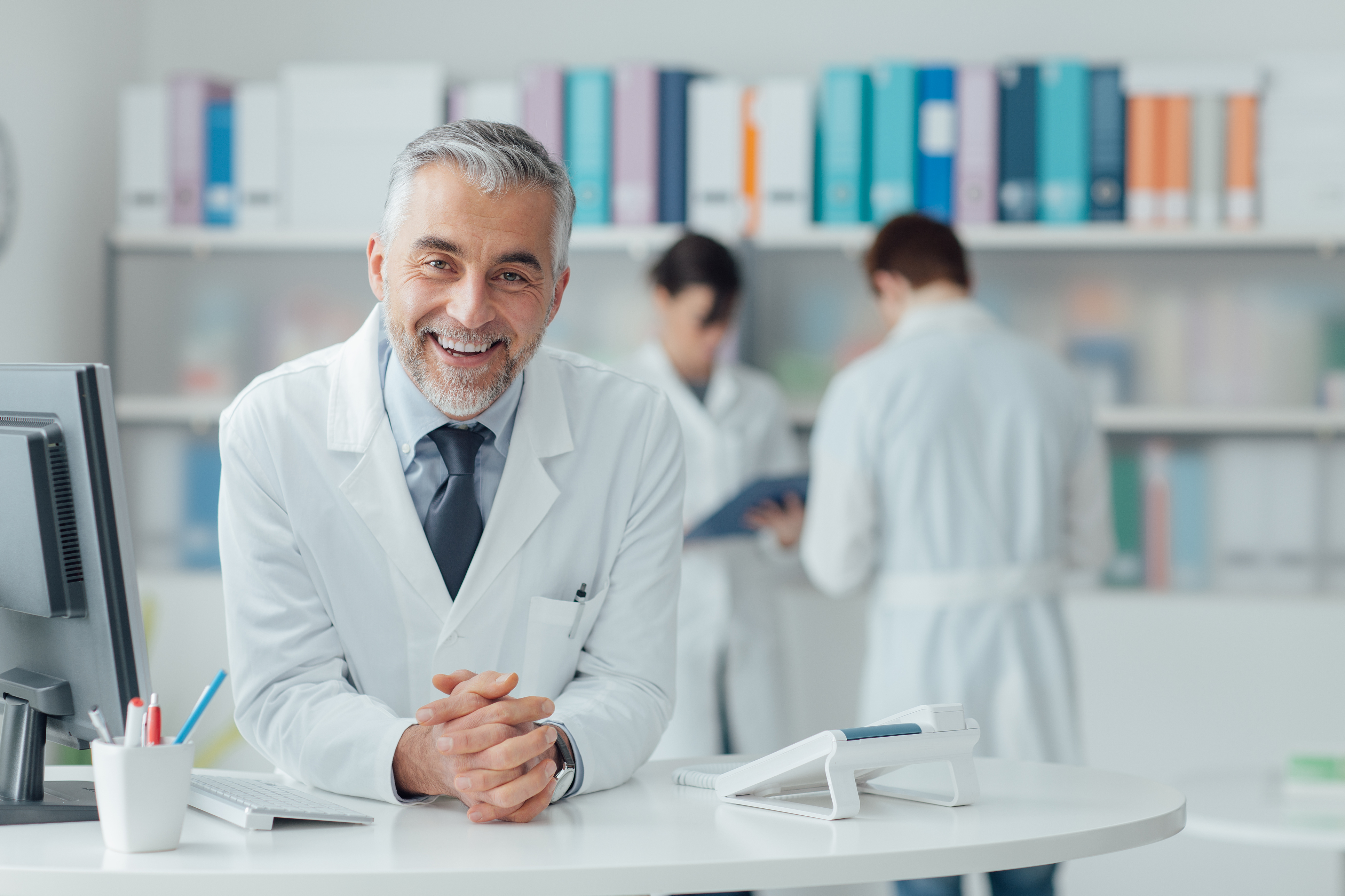 Doctor sitting at his computer with medical staff behind him.